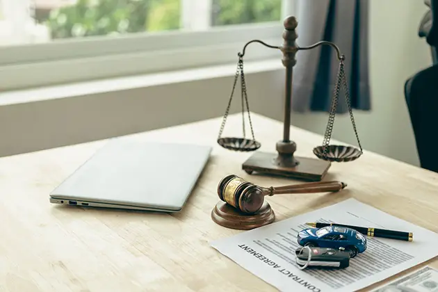 Scales of justice, a gavel and car keys on a desk — how long it takes to settle a personal injury claim
